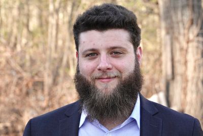 Smiling man with a full beard wearing a suit jacket outdoors.