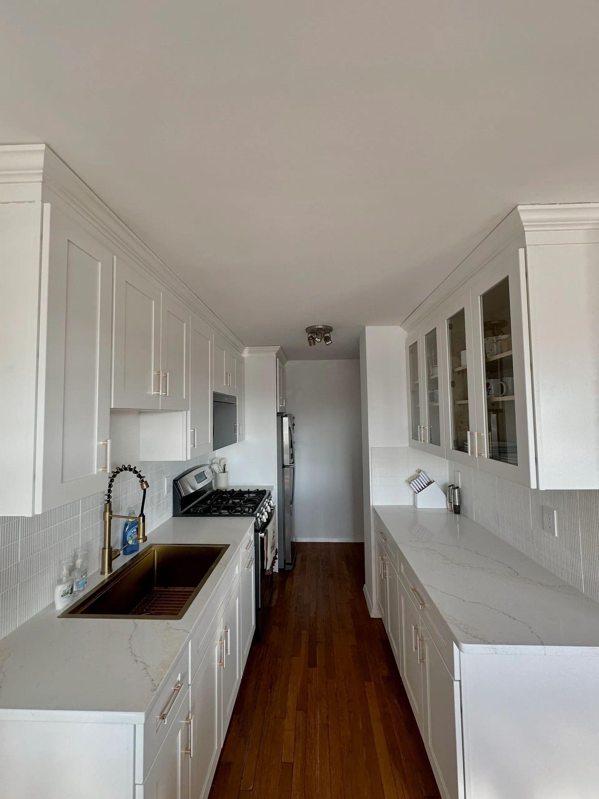 Modern galley kitchen with white cabinetry and wooden floor.