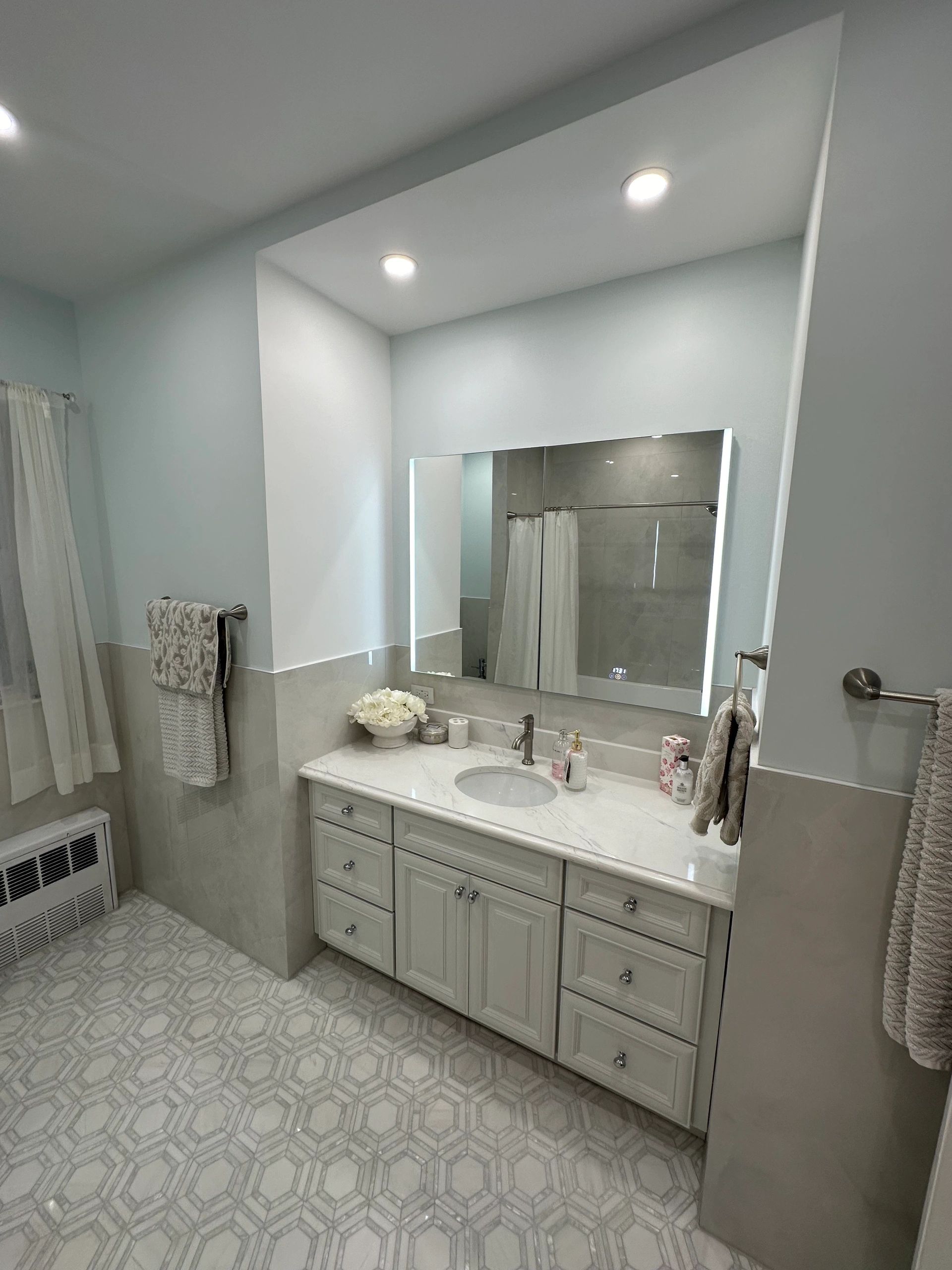 Modern bathroom vanity with illuminated mirror and patterned floor tiles.