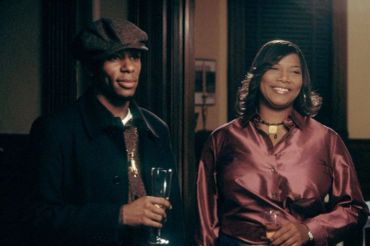 A man and woman smiling indoors, dressed stylishly.