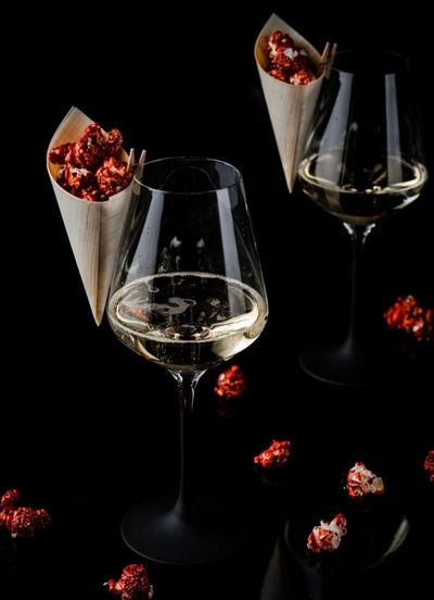 Elegant glasses of white wine with cones of red popcorn on a black background.