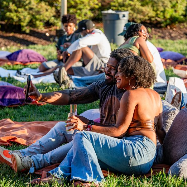 Couple taking a selfie while sitting on the grass during a sunny day outdoors.