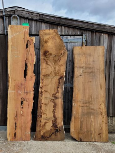 Three large, rustic wooden slabs standing against a weathered shed.