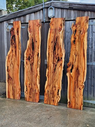 Four polished wooden slabs with natural grain patterns leaning against a shed.
