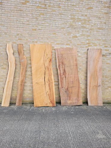 Five wooden planks of varying shapes and sizes leaning against a brick wall outdoors.