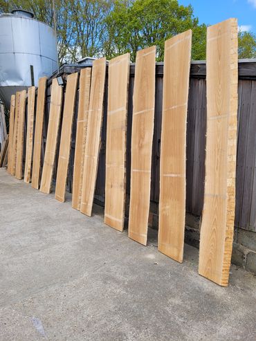 Wooden planks lined up against a fence outdoors on a sunny day.