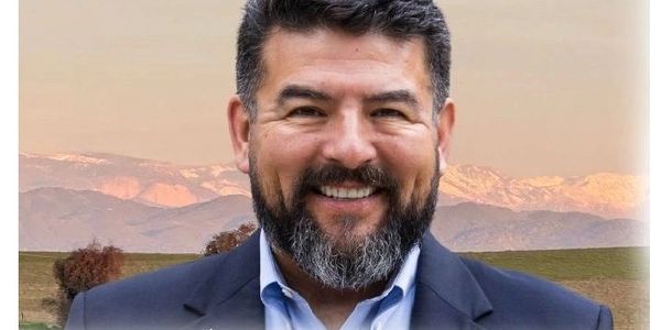 Smiling bearded man in suit with mountains in the background.