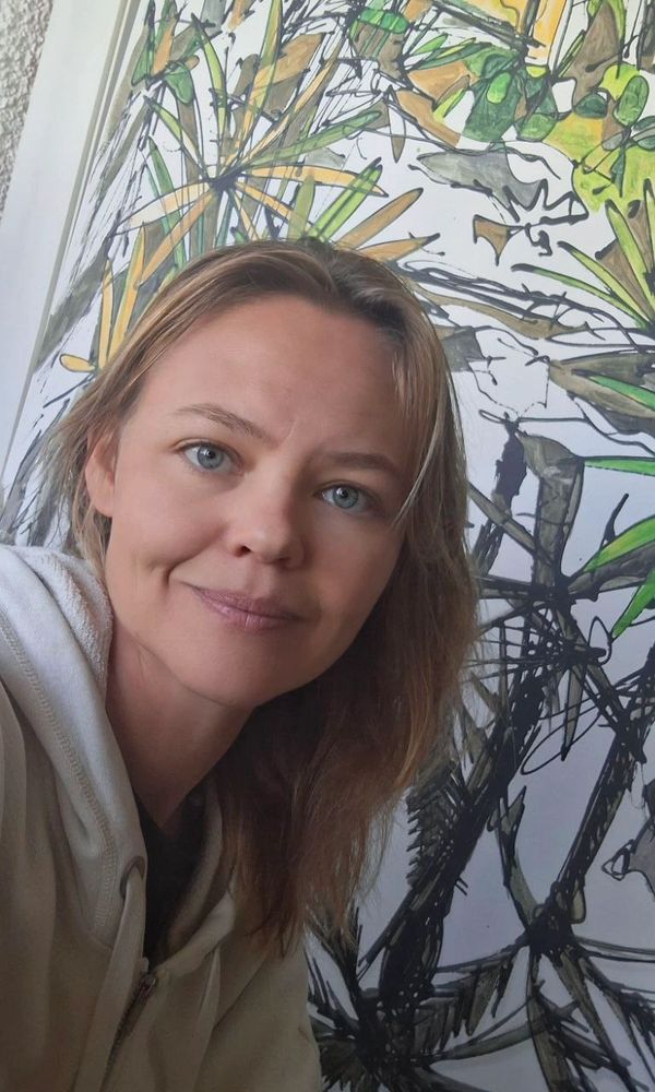 A woman with blue eyes and light brown hair poses in front of an abstract painting.