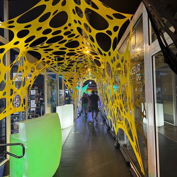 Passage en forme de tunnel décoré de tissu jaune en toile d’araignée et de mobilier illuminé.