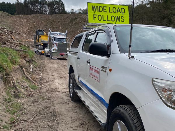 KENWORTH oversize truck with forestry machinery loaded wide load follows pilot vehicle waikato