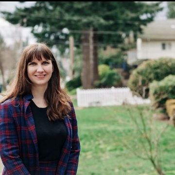 Leah Griffin wearing a plaid jacket and smiling in front of a green lawn with a large fir tree.