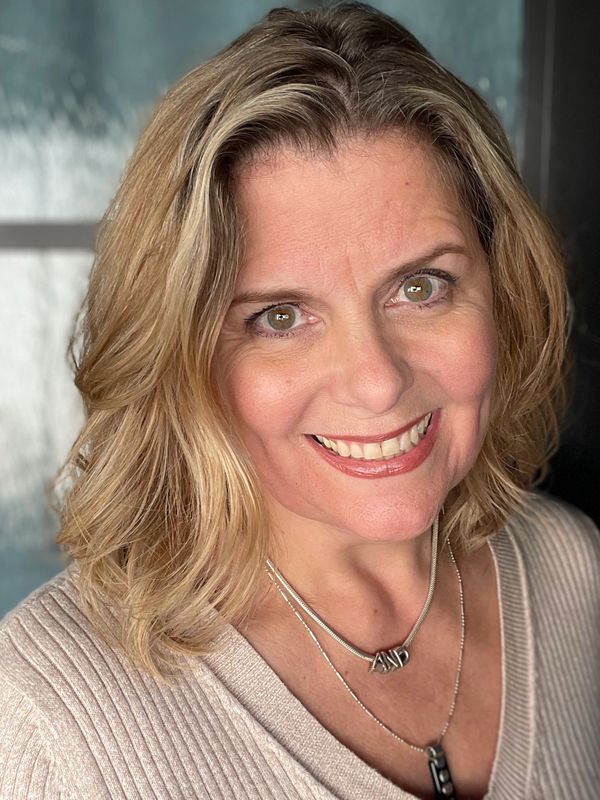 Smiling woman with blonde hair and layered necklaces.