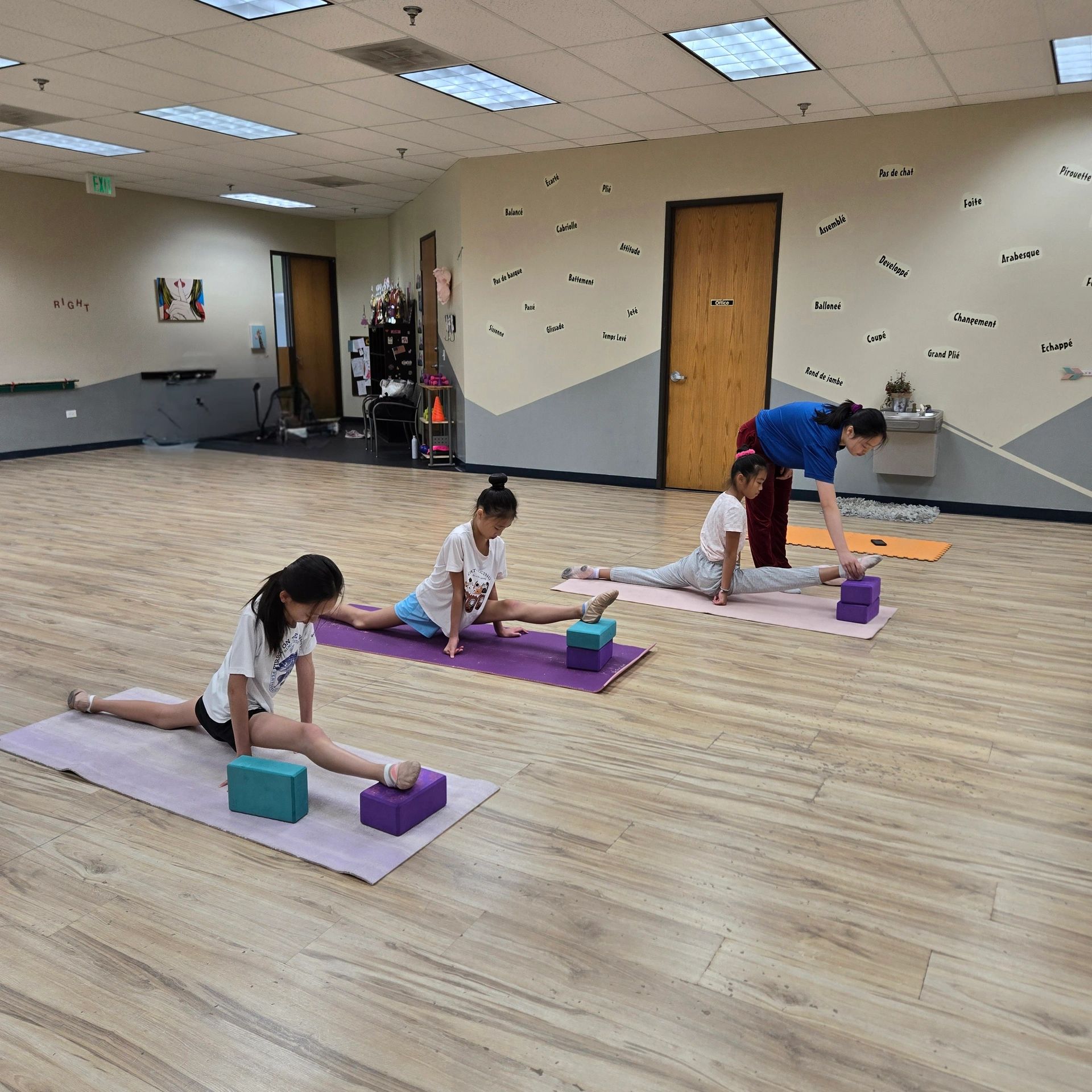 Kids practicing stretching with a teacher in a dance studio.
