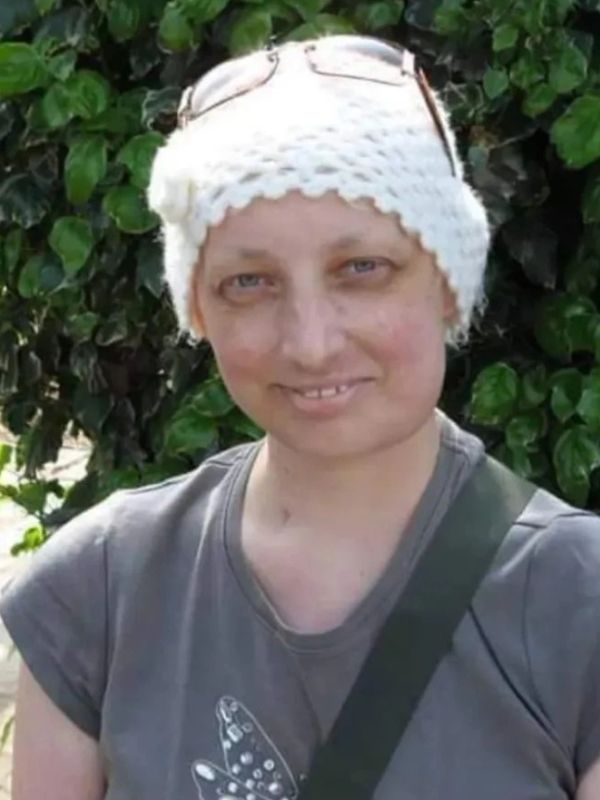 A smiling woman wearing a white knit hat and glasses on her head.