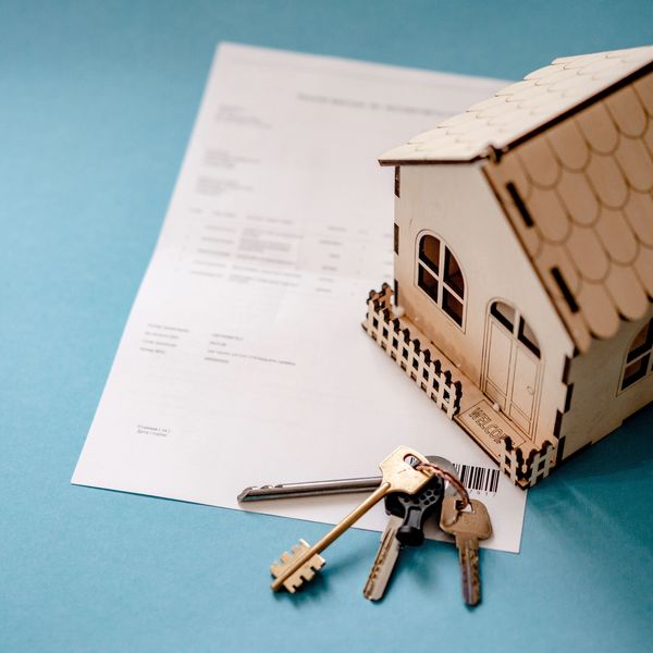 A miniature wooden house with keys and a document on a blue surface.