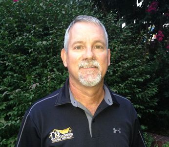Middle-aged man with gray hair and beard in a black polo shirt outdoors.