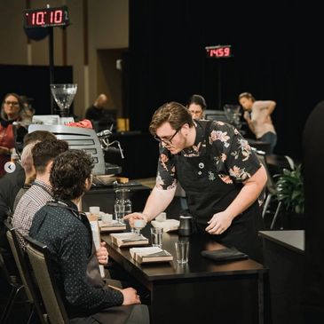 Barista presenting a coffee cup to judges in a competition setting.