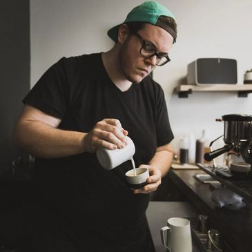 Barista pouring milk into a cup, preparing coffee.