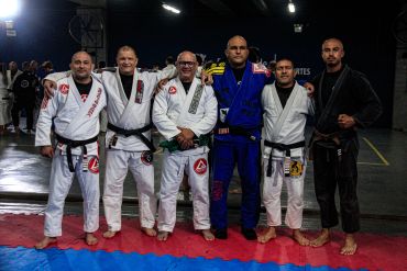 Grupo de homens em kimonos de jiu-jitsu posando em academia.
