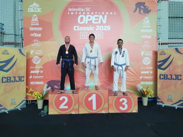 Three Brazilian Jiu-Jitsu competitors on a winners' podium at Joinville Open 2026.