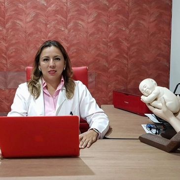 Female doctor sitting at desk with red laptop and baby statue.