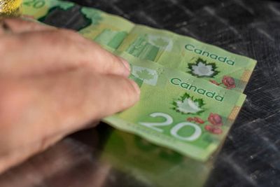 Hand holding Canadian twenty-dollar bills on a reflective surface.