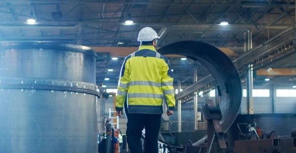 Worker in safety gear inspecting large industrial equipment inside a factory.
