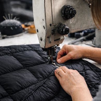 Hands sewing black quilted fabric using a sewing machine.