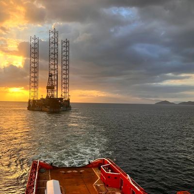 Oil rig platform being towed at sunset over calm sea.