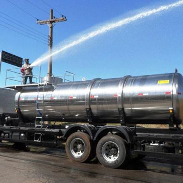 Worker sprays water from a large tanker truck under clear sky.