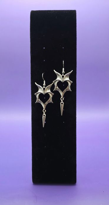 Silver heart-shaped earrings with spikes on a black stand.