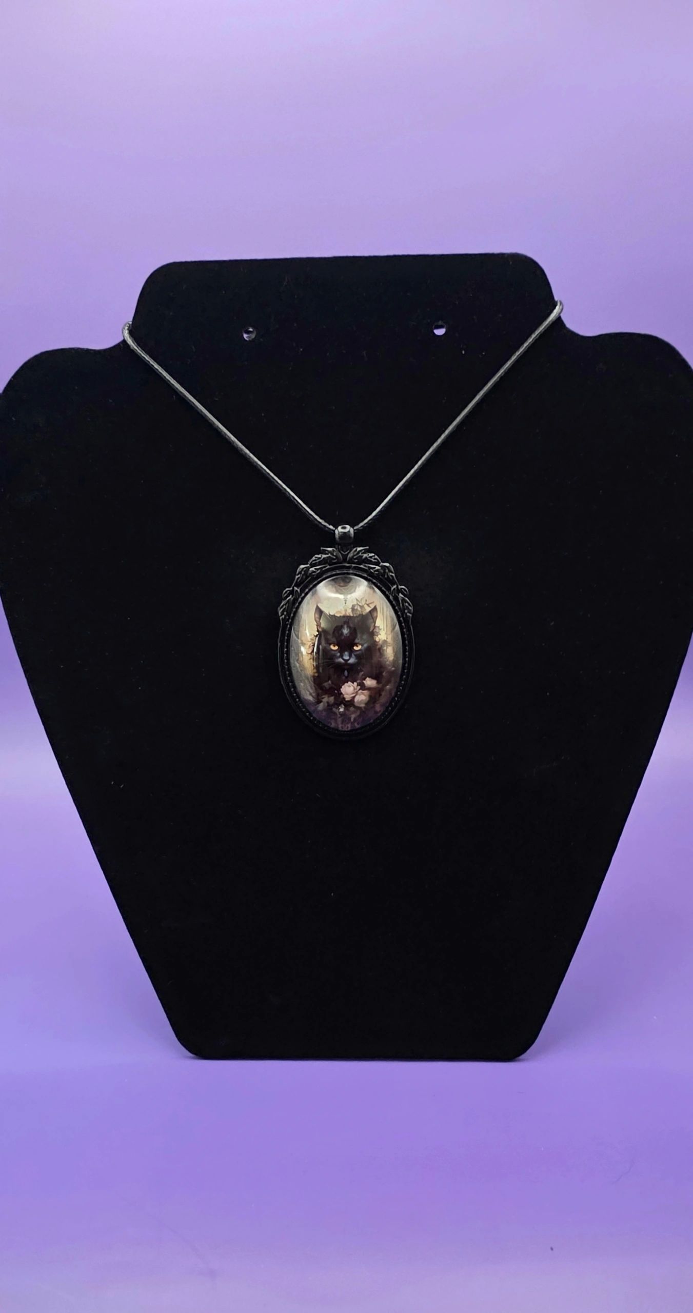 Black cat pendant necklace displayed on a black stand with a purple background.