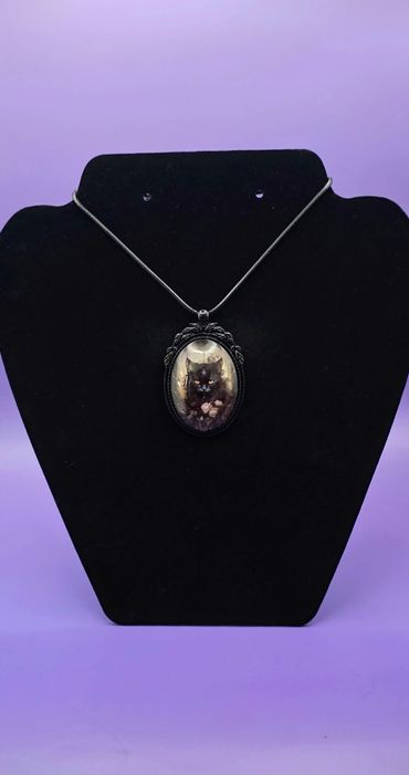 Black cat pendant necklace displayed on a black stand with a purple background.