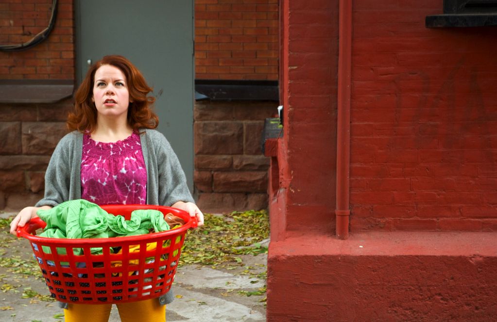 Woman holding a laundry basket outdoors near a red brick wall.