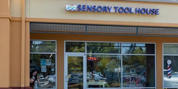 Front of a store that says Sensory Tool House. Two people smiling from behind a post.