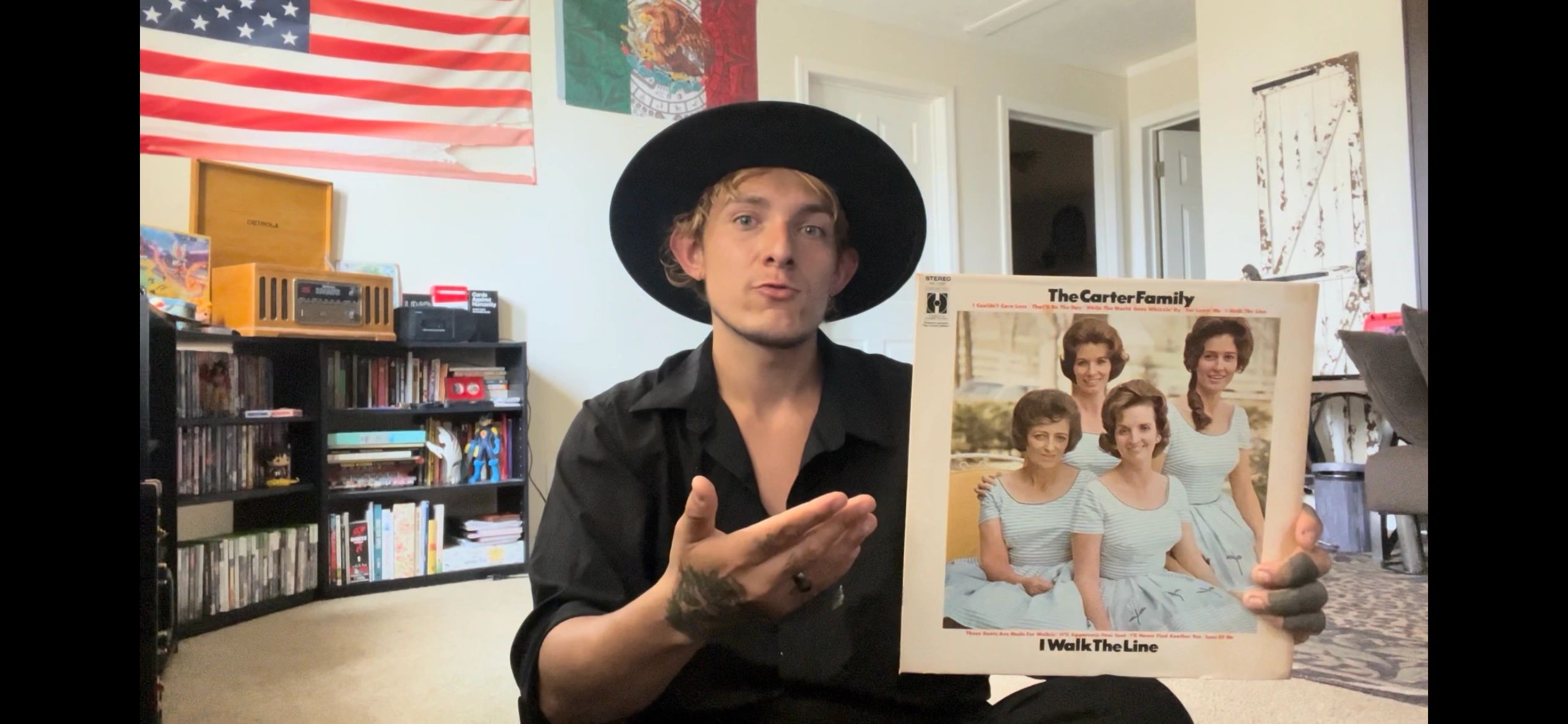 A man in a black hat shows a vintage vinyl album by The Carter Family.