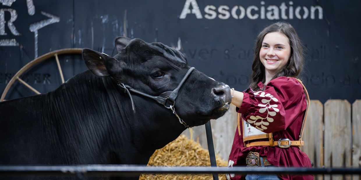 Young woman smiling beside a black cow at an agricultural event.