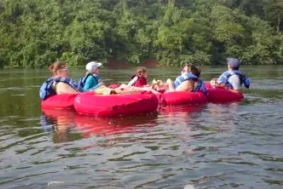 Five people floating on red tubes in a river.
