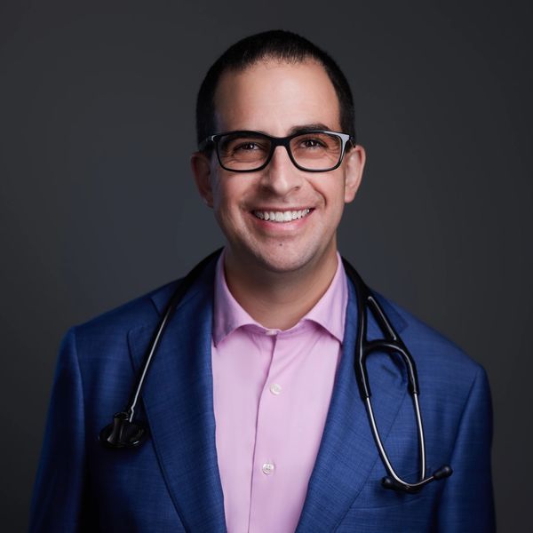 Smiling male doctor in glasses wearing a blue suit and stethoscope.