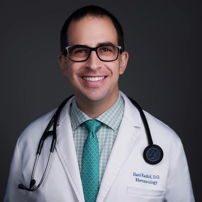Smiling male doctor in white coat with stethoscope and teal tie.