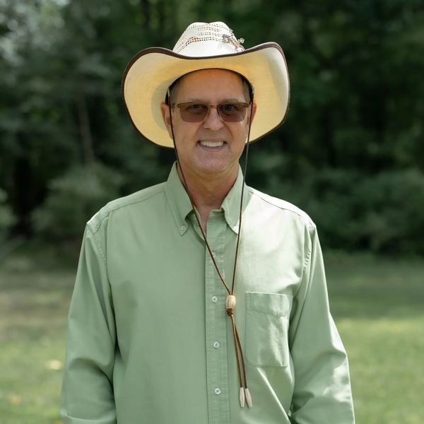 Man in a cowboy hat and green shirt smiling outdoors.