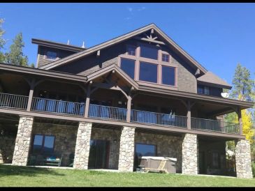 Large house with stone pillars and wooden balcony under blue sky.