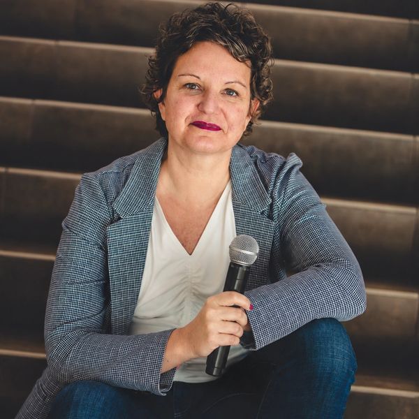 Woman sitting on stairs holding a microphone and smiling.