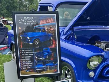 Blue 1957 Chevrolet car at a show with display board.