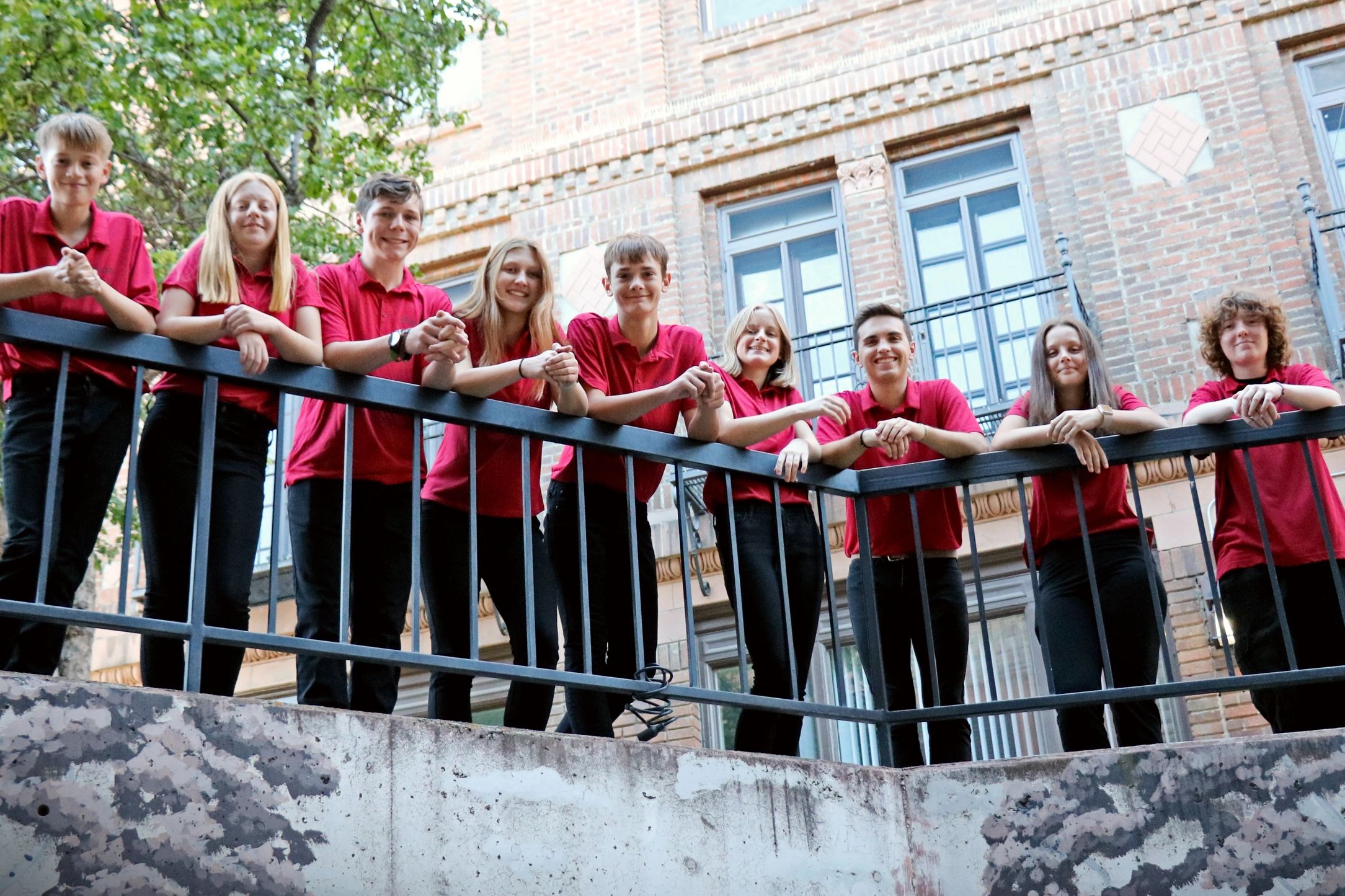 A group of students in red shirts smiling on a balcony.