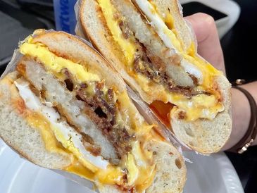 Close-up of a breakfast sandwich with eggs, cheese, and bacon inside a bun.