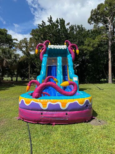 Inflatable water slide decorated with pink flamingos in a sunny park.