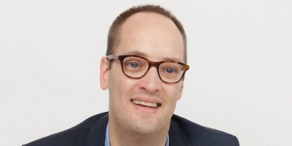 Man with glasses smiling against a plain background.