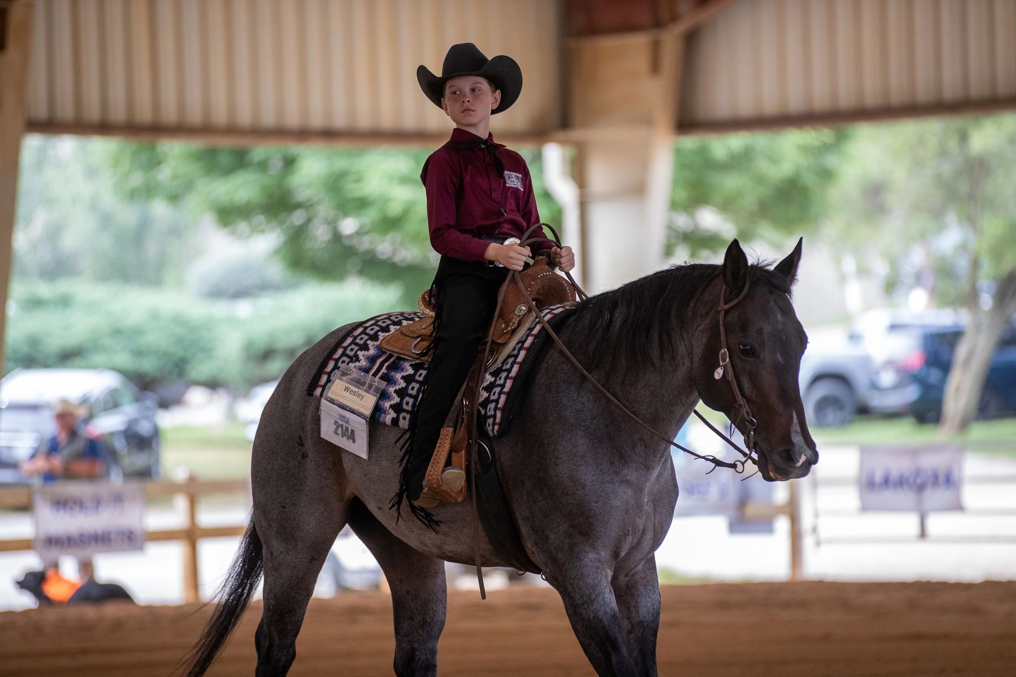 Boy in cowboy attire riding a horse indoors.