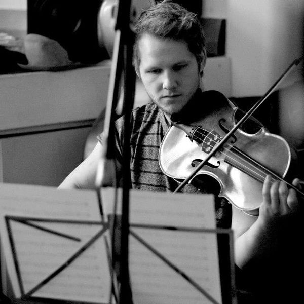 A young man intensely playing the violin while reading sheet music.